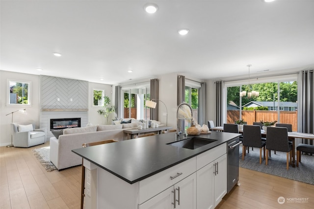 kitchen with sink, white cabinets, a fireplace, an island with sink, and hanging light fixtures