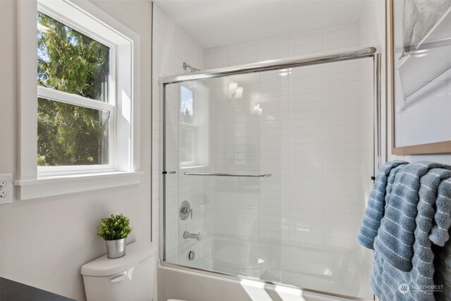 bathroom with toilet, shower / bath combination with glass door, and a healthy amount of sunlight