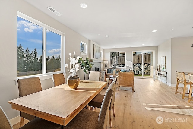 dining room featuring a brick fireplace, a healthy amount of sunlight, and light hardwood / wood-style flooring