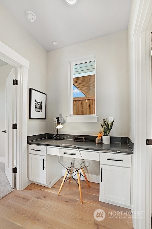 bar featuring white cabinets, light hardwood / wood-style flooring, and built in desk