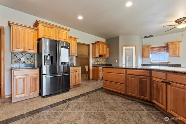 kitchen with ceiling fan, dark tile patterned flooring, dark stone countertops, decorative backsplash, and stainless steel fridge