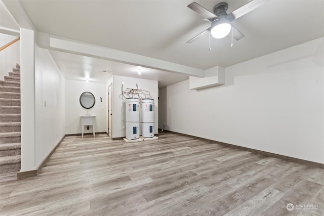 basement featuring ceiling fan, sink, water heater, and light wood-type flooring