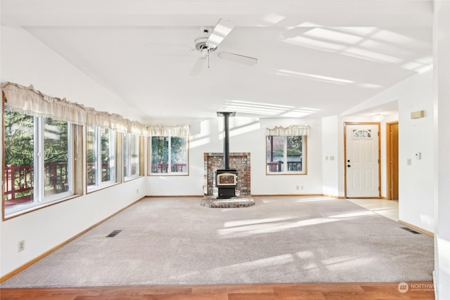 unfurnished living room with ceiling fan, vaulted ceiling, light carpet, and a wood stove