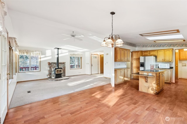 kitchen with pendant lighting, white appliances, light hardwood / wood-style flooring, a center island, and a wood stove