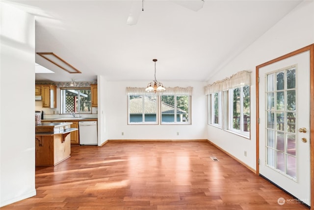 unfurnished dining area featuring sink, vaulted ceiling, a chandelier, and light wood-type flooring