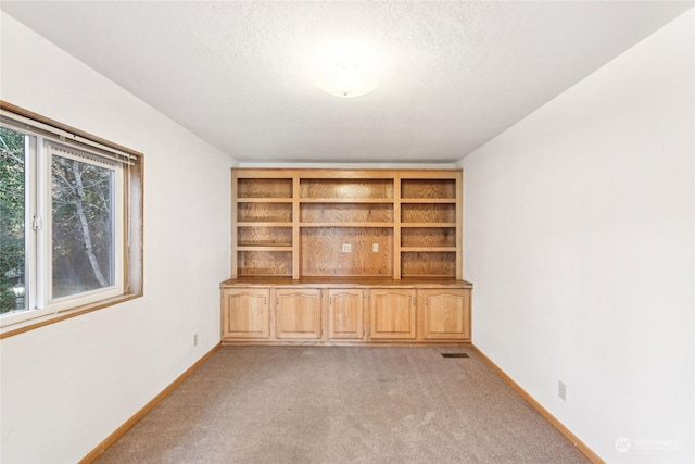 unfurnished living room featuring built in shelves, light colored carpet, and a textured ceiling