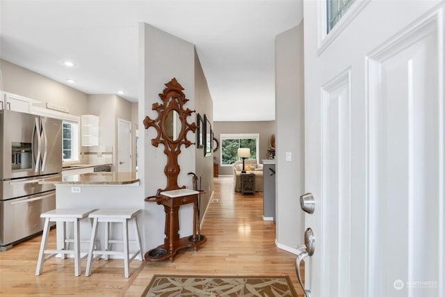 kitchen with tasteful backsplash, white cabinetry, stainless steel fridge, light stone countertops, and light hardwood / wood-style flooring