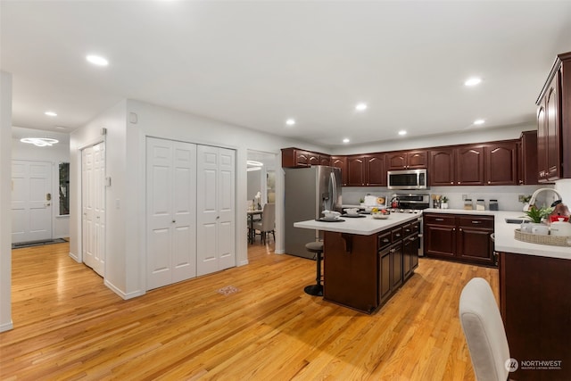 kitchen with a kitchen breakfast bar, appliances with stainless steel finishes, light wood-type flooring, a center island, and sink