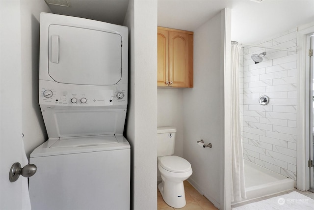 bathroom featuring stacked washer and clothes dryer, tile patterned flooring, curtained shower, and toilet