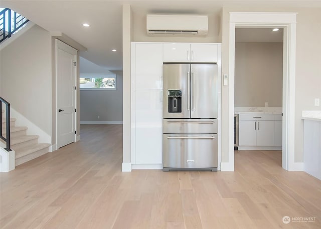 kitchen with a wall unit AC, white cabinets, high quality fridge, and light hardwood / wood-style floors