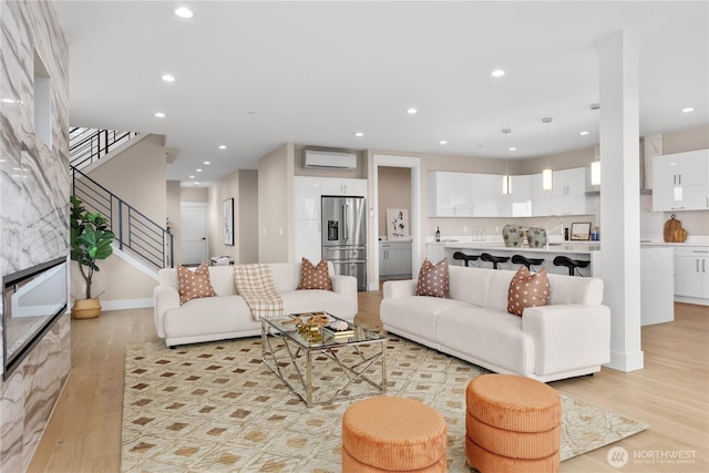 living area featuring a wall unit AC, baseboards, recessed lighting, stairs, and light wood-style floors