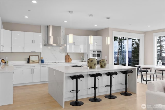 kitchen with a kitchen breakfast bar, black electric stovetop, wall chimney exhaust hood, and an island with sink