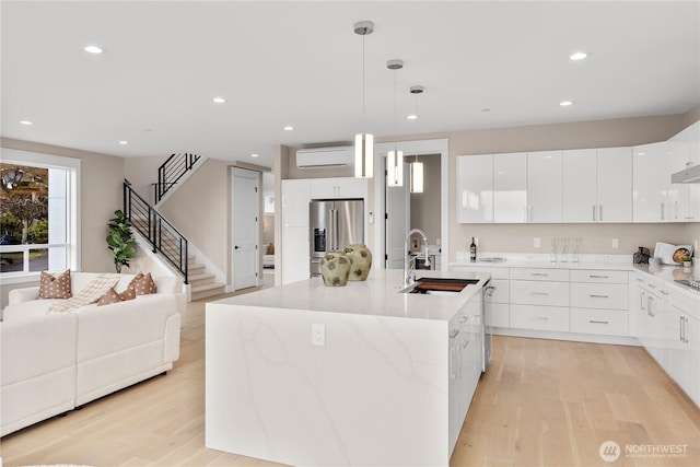 kitchen with modern cabinets, an AC wall unit, light wood-style flooring, a sink, and high end refrigerator