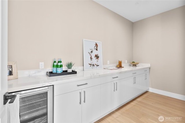 bar featuring light wood-style flooring, baseboards, and beverage cooler