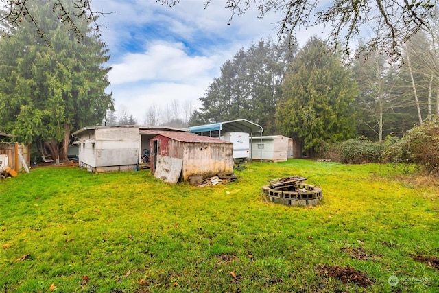 view of yard with an outdoor fire pit, a carport, and a storage unit