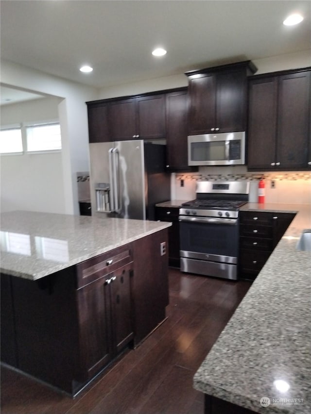 kitchen with light stone counters, dark brown cabinetry, appliances with stainless steel finishes, and dark hardwood / wood-style flooring