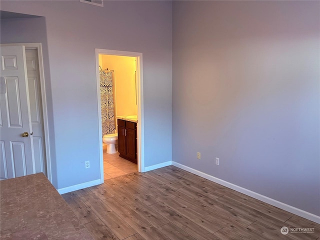 unfurnished bedroom with light hardwood / wood-style flooring, a closet, ensuite bath, and a walk in closet