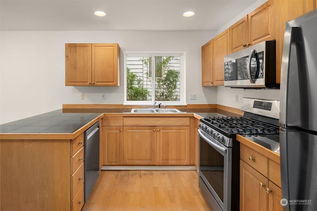 kitchen with appliances with stainless steel finishes, tile countertops, light hardwood / wood-style flooring, and sink