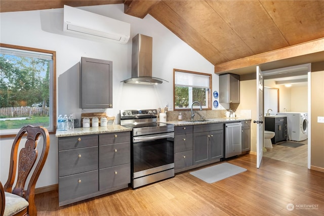 kitchen featuring stainless steel appliances, sink, gray cabinets, wall chimney range hood, and a wall mounted air conditioner