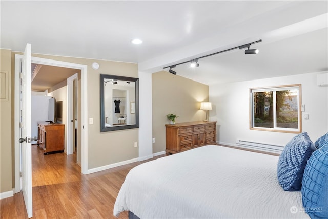 bedroom with light hardwood / wood-style floors, baseboard heating, a wall mounted air conditioner, and rail lighting