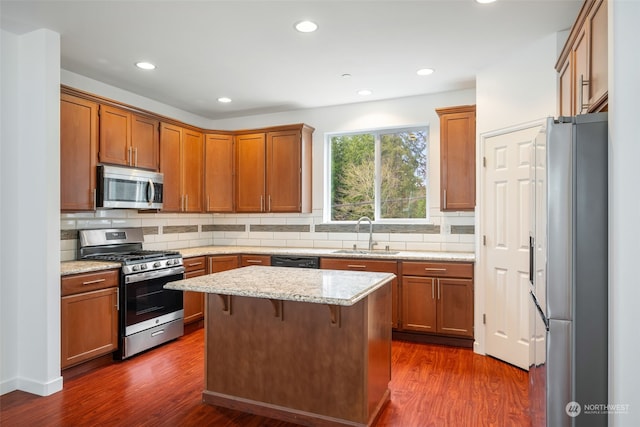 kitchen featuring light stone counters, a center island, stainless steel appliances, dark hardwood / wood-style flooring, and sink