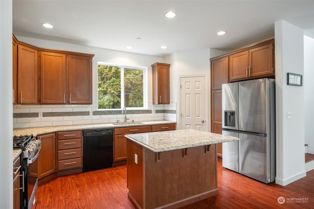 kitchen featuring appliances with stainless steel finishes, a center island, light stone counters, dark hardwood / wood-style floors, and sink