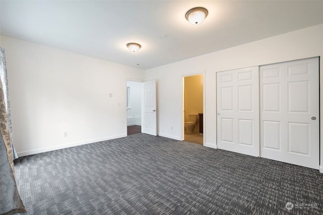 unfurnished bedroom featuring a closet, ensuite bath, and dark carpet