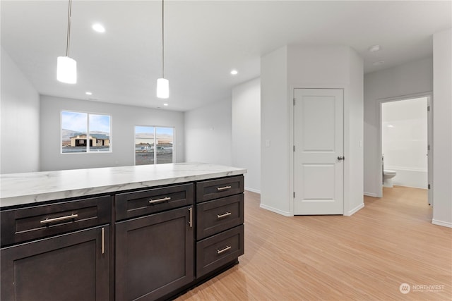 kitchen with decorative light fixtures, dark brown cabinetry, light stone counters, and light hardwood / wood-style floors