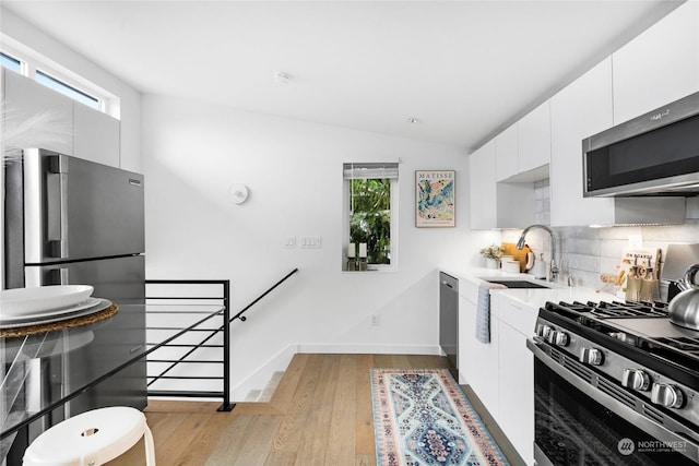 kitchen with lofted ceiling, backsplash, white cabinetry, appliances with stainless steel finishes, and sink