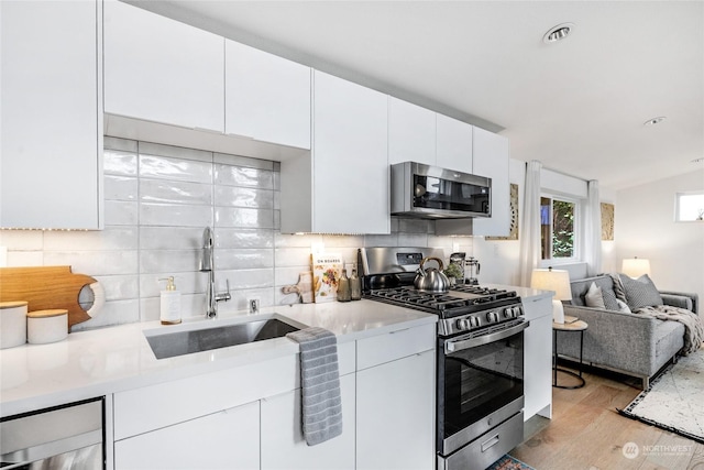 kitchen featuring lofted ceiling, light wood-type flooring, white cabinetry, appliances with stainless steel finishes, and sink