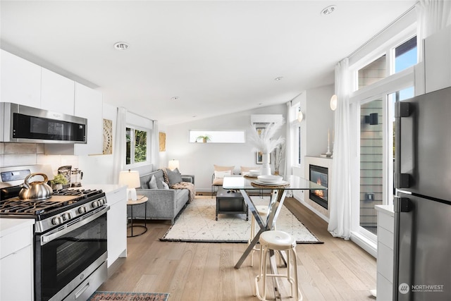 kitchen with stainless steel appliances, white cabinetry, vaulted ceiling, light hardwood / wood-style floors, and tasteful backsplash