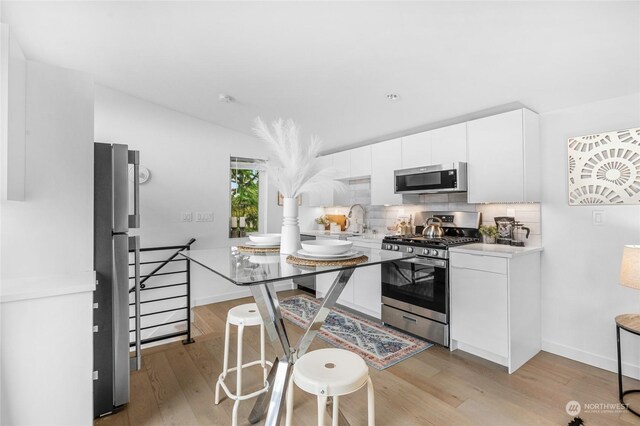 kitchen featuring stainless steel appliances, white cabinetry, lofted ceiling, light hardwood / wood-style floors, and decorative backsplash