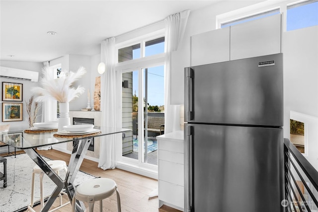 kitchen with white cabinets, stainless steel fridge, light wood-type flooring, and an AC wall unit