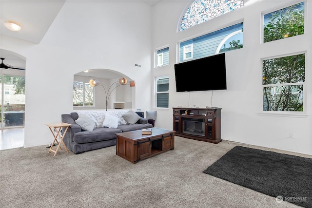 living room featuring a towering ceiling, ceiling fan, and light carpet