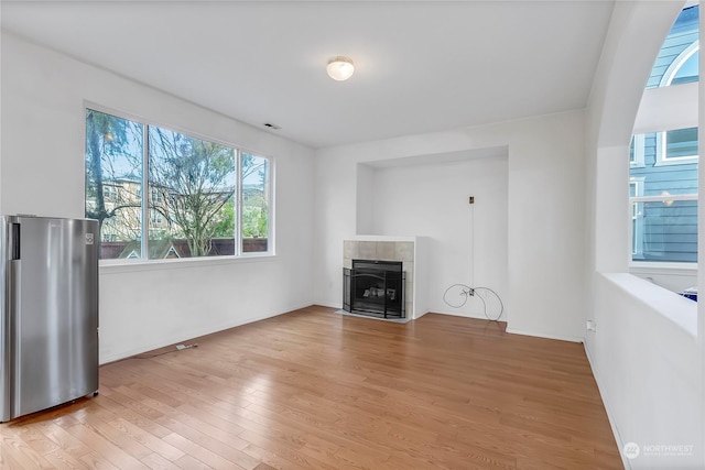 unfurnished living room featuring light hardwood / wood-style floors and a tiled fireplace