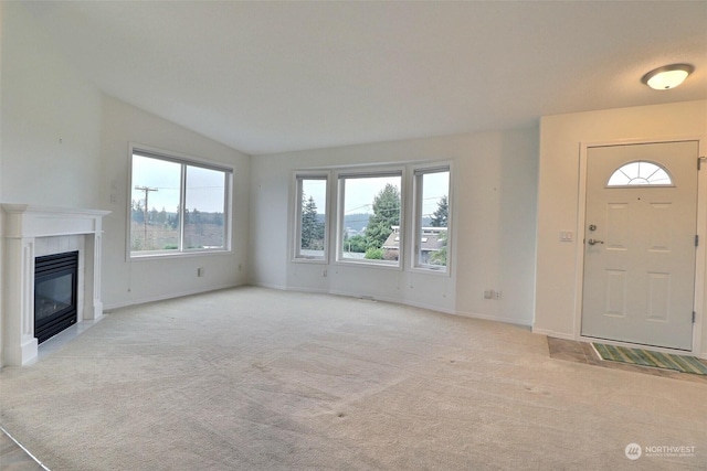 unfurnished living room with light colored carpet, lofted ceiling, a tiled fireplace, and a healthy amount of sunlight