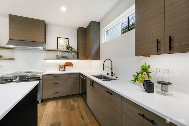 kitchen featuring decorative backsplash, light wood-type flooring, wall chimney range hood, stainless steel stove, and sink