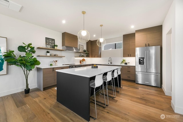 kitchen with high quality fridge, a kitchen island, decorative light fixtures, light hardwood / wood-style floors, and a breakfast bar