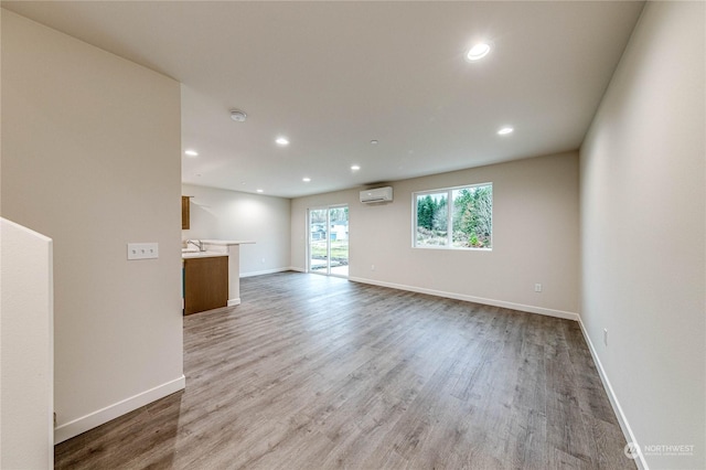 unfurnished living room featuring sink, light hardwood / wood-style flooring, and a wall mounted AC