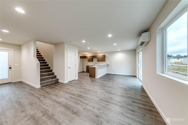 unfurnished living room featuring wood-type flooring, plenty of natural light, and a wall mounted air conditioner