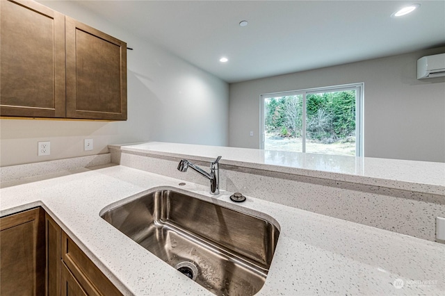 kitchen featuring sink, a wall mounted AC, and light stone counters