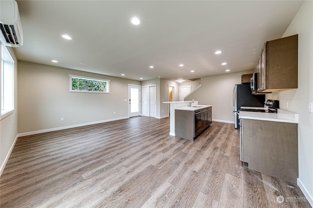 kitchen with a center island with sink, light wood-type flooring, stove, an AC wall unit, and sink