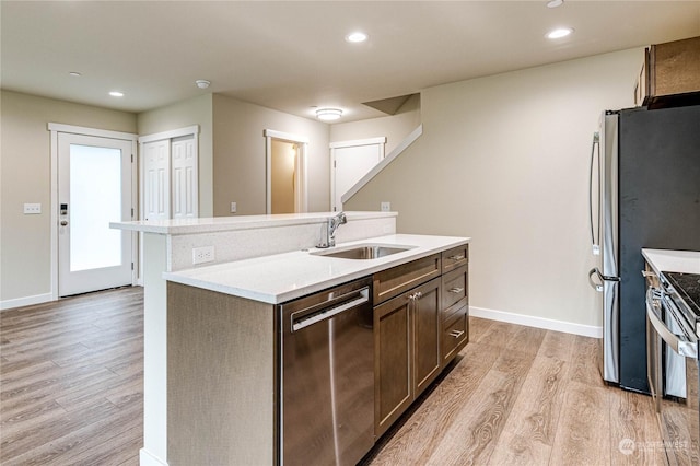 kitchen featuring an island with sink, stainless steel appliances, light wood-type flooring, dark brown cabinets, and sink