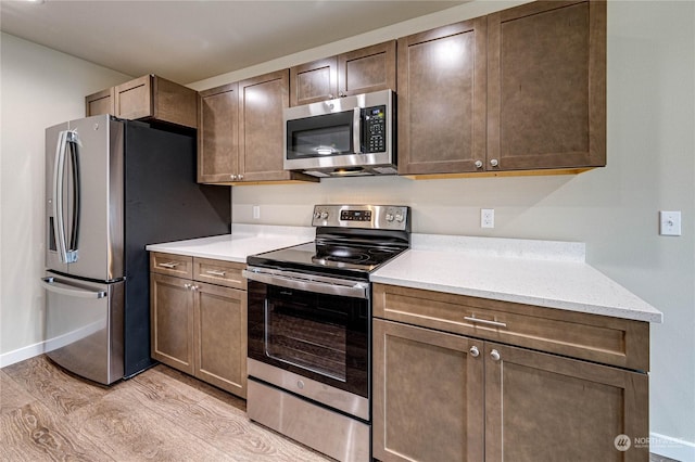 kitchen with appliances with stainless steel finishes, light stone counters, and light hardwood / wood-style floors