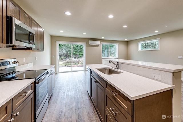 kitchen featuring sink, light hardwood / wood-style flooring, a wall mounted air conditioner, appliances with stainless steel finishes, and an island with sink