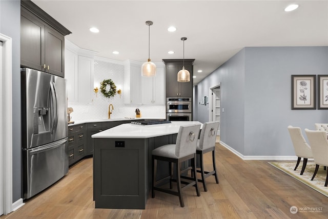 kitchen featuring a center island, hanging light fixtures, light wood-type flooring, white cabinetry, and appliances with stainless steel finishes