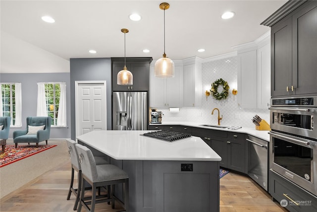 kitchen with stainless steel appliances, decorative light fixtures, white cabinets, light hardwood / wood-style flooring, and a kitchen island