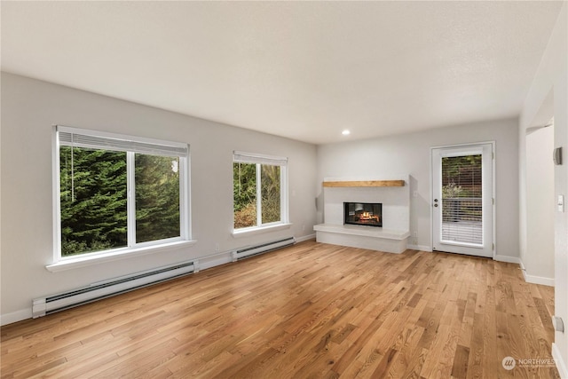 unfurnished living room featuring light hardwood / wood-style floors, baseboard heating, and plenty of natural light