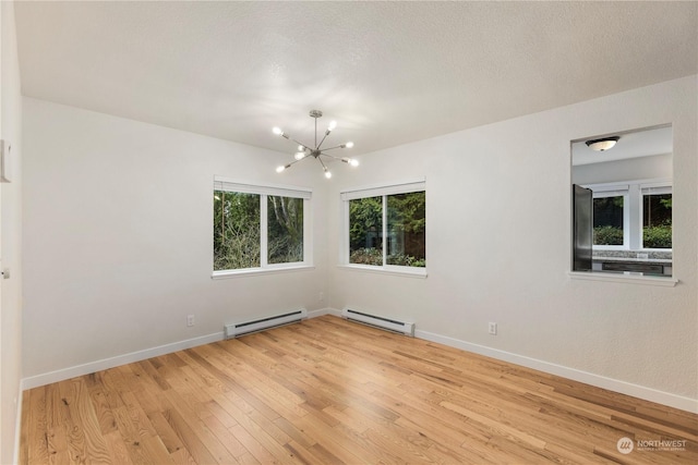 empty room featuring a baseboard heating unit, light wood-type flooring, and a chandelier