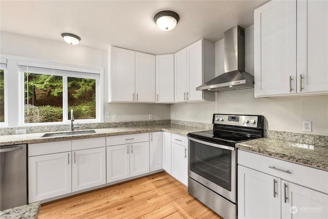 kitchen featuring white cabinetry, appliances with stainless steel finishes, sink, light hardwood / wood-style flooring, and wall chimney range hood